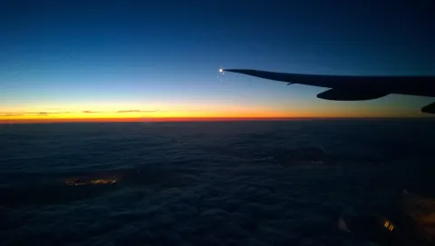 Aircraft wing above the clouds at sunset, seen from a passenger window
