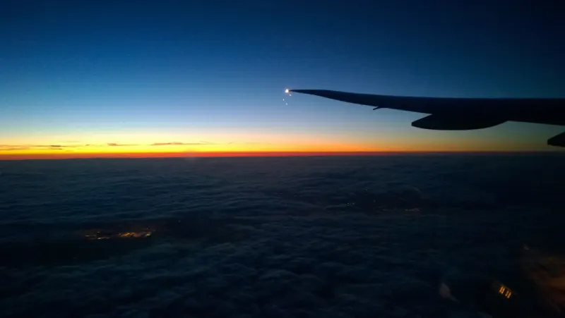 Aircraft wing above the clouds at sunset, seen from a passenger window